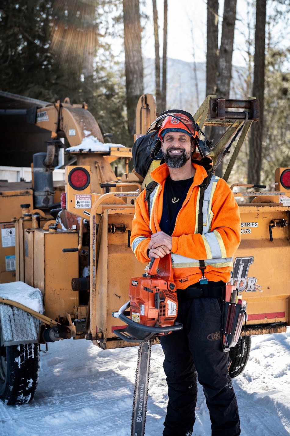 Ian Elshaw in full safety gear holding a chainsaw beside the wood chipper